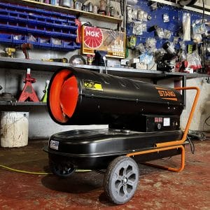 Stang Blow Kerosene Heaters- 20KW & 30KW-2 A Stang Blow Paraffin Heater (20KW or 30KW) on wheels sits in a workshop with shelves and toolsโideal for tool hire Newry customers needing effective on-site heating.