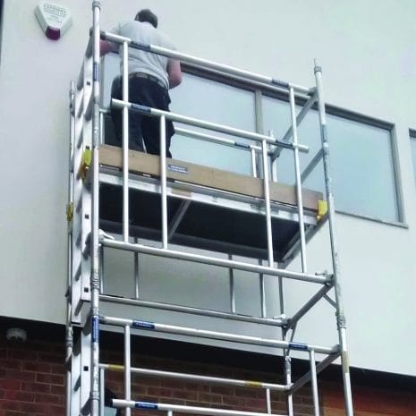 Aluminium Scaffold-2 A person stands on an Aluminium Scaffold from tool hire Newry, working near a window on the building’s upper storey.