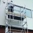 A person stands on an Aluminium Scaffold from tool hire Newry, working near a window on the building’s upper storey.
