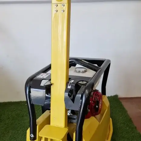Cargo PB60 5.5hp Vibrating Whacker Plate-6 A Cargo PB60 5.5hp Vibrating Wacker Plate with black handles sits on artificial green grass indoors against a white wall—available now for tool hire in Newry.