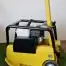 A Cargo PB60 5.5hp Vibrating Wacker Plate in yellow and black with a metal handle is set on artificial grass indoors by an electrical socket, available for tool hire in Newry.