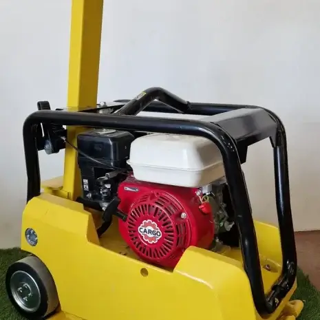 Cargo PB60 5.5hp Vibrating Whacker Plate-4 A Cargo PB60 5.5hp Vibrating Wacker Plate with a red engine, available for tool hire Newry, is shown on artificial grass indoors, beside a white wall and power socket.