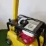 The Cargo PB60 5.5hp Vibrating Wacker Plate features a yellow body, red engine, and black handles, with a control panel. Available for tool hire Newry; pictured on artificial grass by a white wall.