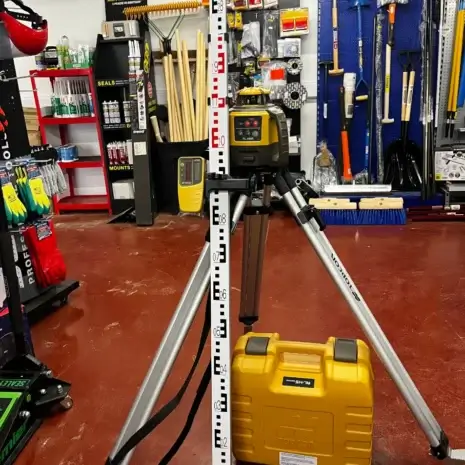 Topcon RL-H5A Rotating Laser Level-4 A laser level on a tripod is set up next to a levelling rod and a yellow equipment case in a hardware store aisle, showcasing tools and supplies available for tool hire Newry customers.