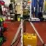 A laser level on a tripod is set up next to a levelling rod and a yellow equipment case in a hardware store aisle, showcasing tools and supplies available for tool hire Newry customers.