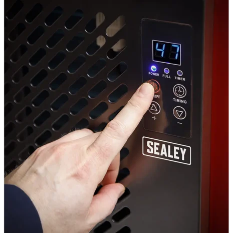 Sealey 70L Industrial Dehumidifier SDH70-5 A hand presses the power button on a Sealey 70L Industrial Dehumidifier SDH70—available for hire in Newry—with a digital display reading 47 and multiple control buttons.