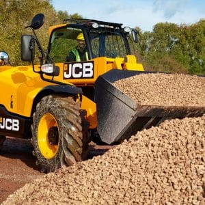 A yellow JCB 531-70 Telehandler with a front bucket moves gravel at a tree-lined, dirt-filled construction site—a reliable plant hire choice for Newry projects.