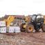 A yellow 531-70 Telescopic handler from tool hire Newry lifts a pallet of white construction blocks at a building site, with houses and materials visible in the background.