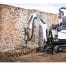 A man uses a Bobcat E10Z Mini Digger with a breaker attachment to break ground by an old brick wall—ideal for those seeking tool hire Newry options.
