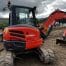 A Kubota U48-4 compact excavator with digging bucket stands on a dirt construction site, hills and clouds behind—perfect for tough tasks and available for hire in Newry.