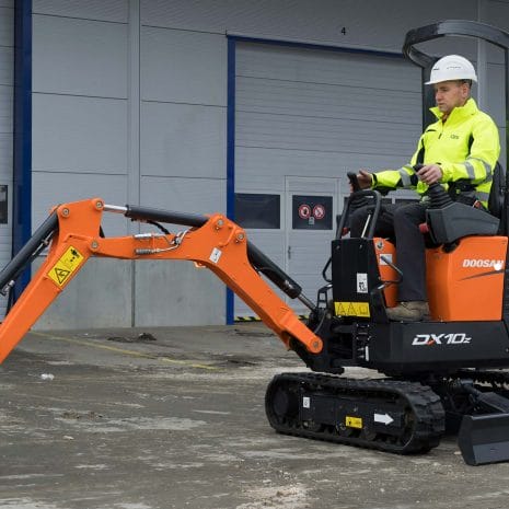 A worker operates a Doosan DX10z Mini Digger on a concrete surface near an industrial building, highlighting dependable equipment offered by tool hire Newry.