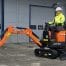 A worker operates a Doosan DX10z Mini Digger on a concrete surface near an industrial building, highlighting dependable equipment offered by tool hire Newry.