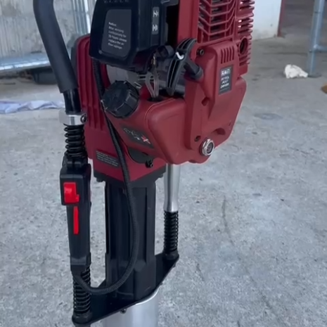 Sealey 2-Stroke Petrol Post Driver 100mm-4 The Sealey 2-Stroke Petrol Post Driver 100mm, featuring a red body with a black handle and control buttons, stands upright on concrete and is available for tool hire in Newry.