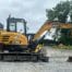 SANY SY50U compact excavator with tracks on gravel near a building and trees under a cloudy sky, available for tool hire in Newry.