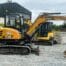 Two SANY SY50U compact excavators, available for tool hire Newry, are parked on gravel near a farm building with trees and stone walls in the background.